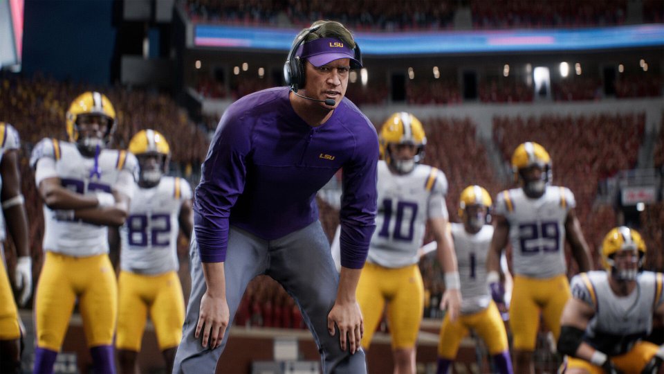 LSU coach in a headset leans forward on the sideline with football players behind him in a College Football 27 stadium scene.