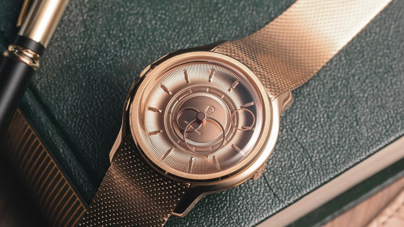A rose-gold luxury watch with a textured dial beside a fountain pen on a dark leather surface