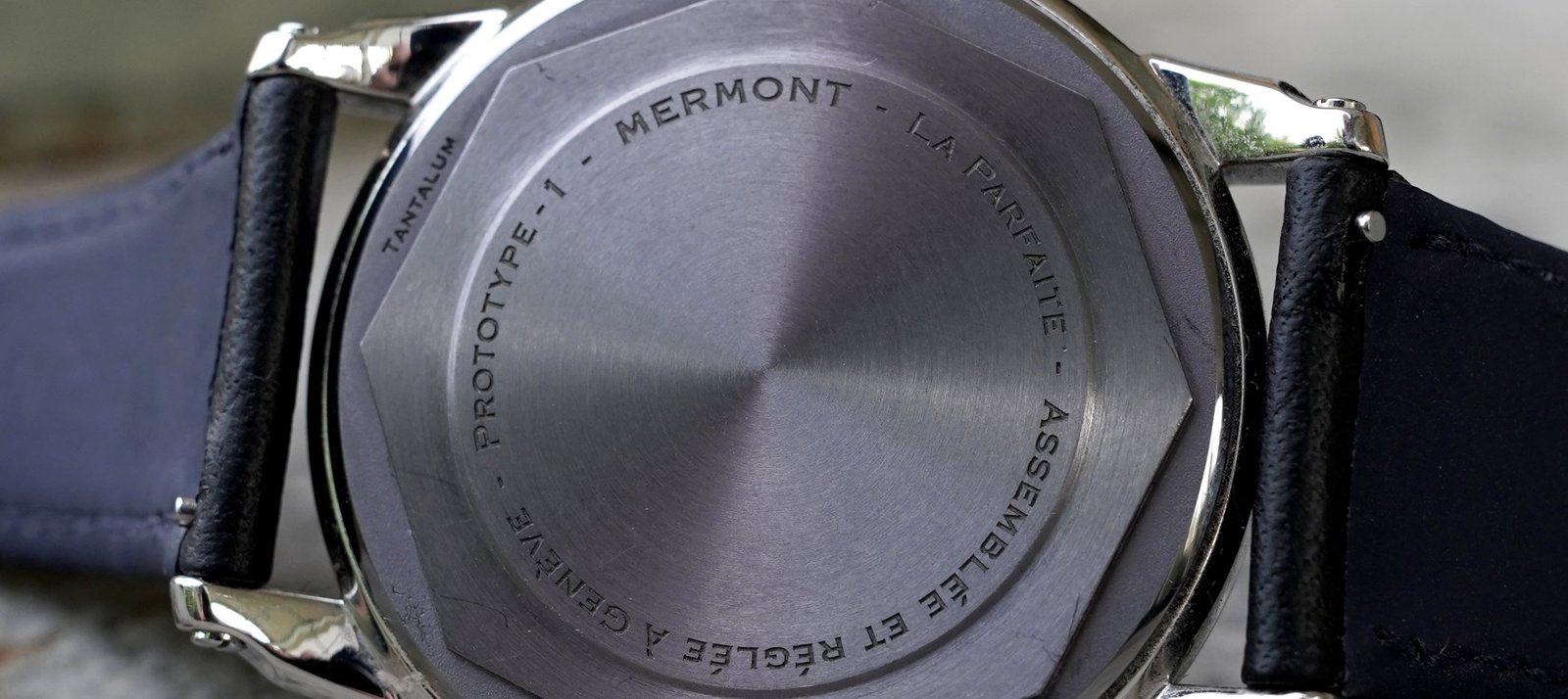 Macro view of a dress watch caseback and black leather strap, showing the case profile and lugs.